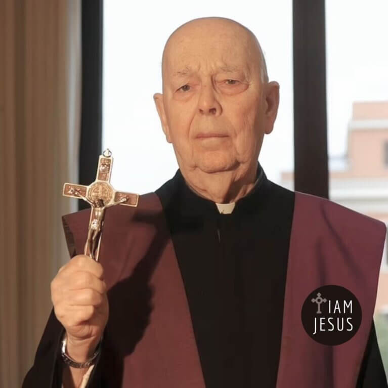Older man in priest robes holding a crucifix, with a circular 'I AM JESUS' badge visible on his chest