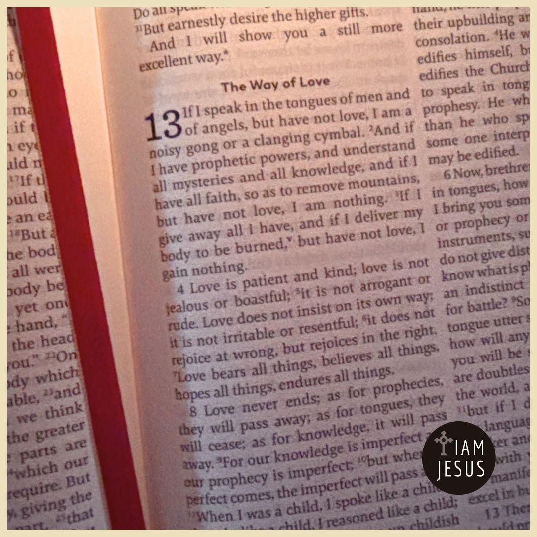 Open Bible page showing chapter 13 'The Way of Love' with dense text, a red gutter margin on the left, and an 'I AM JESUS' circular sticker near the bottom-right.